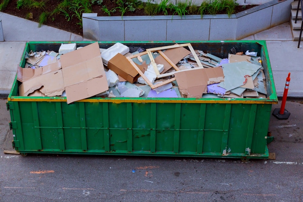 Grüner Container voller Bauschutt, darunter Karton und andere Materialien.
